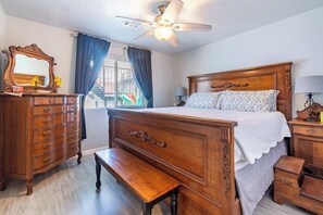 A bedroom with a wooden bed, a dresser, a bench, a ceiling fan, and a window with curtains.
