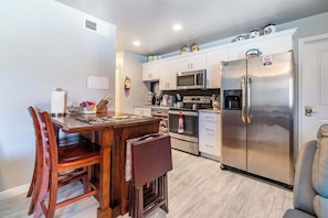 A kitchen with white cabinets, a stainless steel refrigerator, a microwave, an oven, and a dining table with chairs. - Grandma's Southern Comfort Vacation Rental (Hurricane)