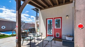 Un espacio de patio cubierto con mobiliario exterior, piscina y una puerta roja.