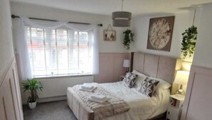 Ein Schlafzimmer mit Bett, Nachttischen, einem Fenster und einer hängenden Pflanze.