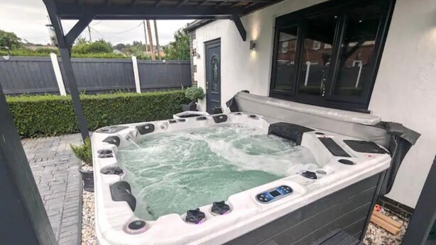 Ein Whirlpool mit Bedienfeld, umgeben von einer Holzterrasse und einem überdachten Bereich.