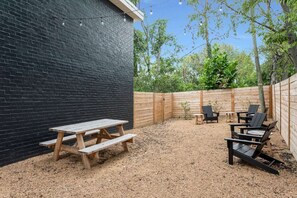 Une cour arrière avec une table de pique-nique et des chaises, une clôture en bois et un mur noir.