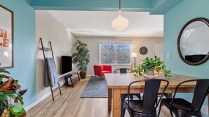 A modern living room with a wooden floor, a dining table with chairs, a red sofa, a large window, and a hanging light fixture. - Vinyl & Velvet w/ Parking near Vandy/DTWN (Nashville)