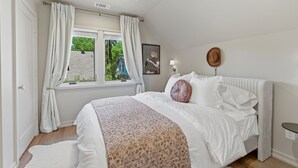 Un dormitorio con cama, ventana con cortinas, ventilador de techo, lámpara de pared y un cuadro enmarcado.