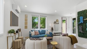 Una sala de estar moderna con un sofá azul, sillones blancos, una mesita de centro y un adorno verde en la pared.