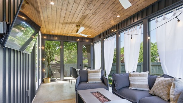 Un espacio de estar al aire libre techado, con techo de madera, ventanas amplias y luces colgantes.