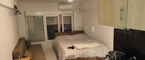 Ein Schlafzimmer mit Bett, Schreibtisch, Stuhl, Kleiderschrank und einem Fenster mit Jalousien.