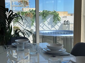 A dining table with clear glassware, a white tablecloth, and a view of a white lattice fence and greenery outside. - Luxury Penthouse 2-bedroom Jacuzzi  in Ix-Xagħra (Ix-Xagħra)