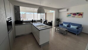 Une cuisine moderne avec un îlot central, un coin repas doté d’un canapé bleu et une grande fenêtre offrant une vue sur le paysage urbain.