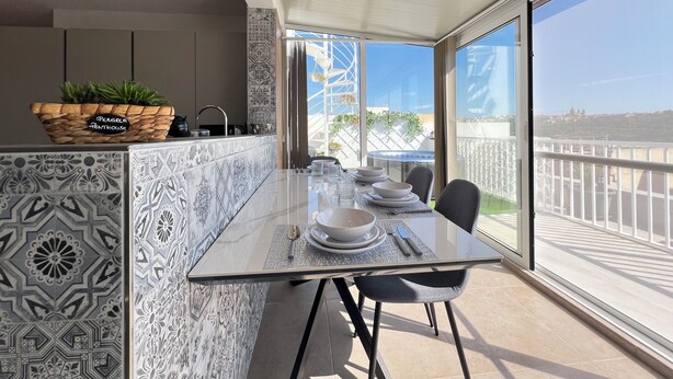 Une cuisine moderne avec un îlot central, un coin repas avec une table en verre et un balcon offrant une vue dégagée.