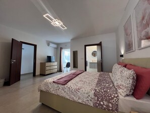 A bedroom with a bed, a dresser, a TV, a chair, and a bathroom visible through an open door. - Luxury Penthouse 2-bedroom Jacuzzi  in Ix-Xagħra (Ix-Xagħra)