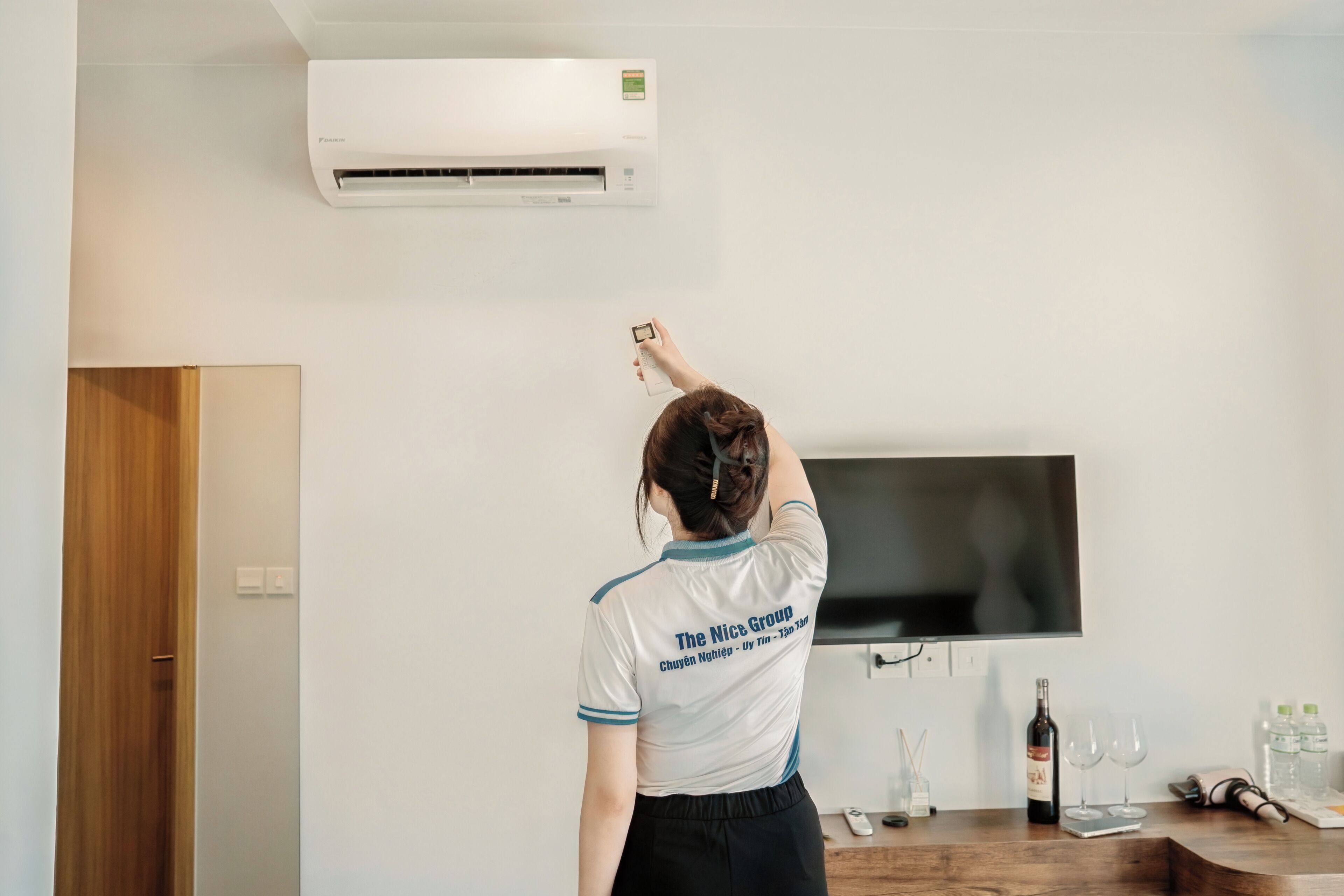 A person in a room with a mounted TV, a wooden door, and a wall-mounted air conditioner.