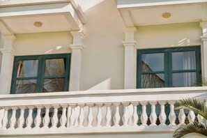 Fachada de edificio con columnas blancas, ventanas con marco verde y balaustrada blanca.