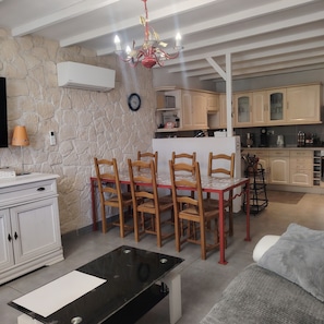 A dining area with a table and chairs, a kitchen with cabinets, and a stone wall. - Nice little house for visiting the little province and the Camargue. (Arles)
