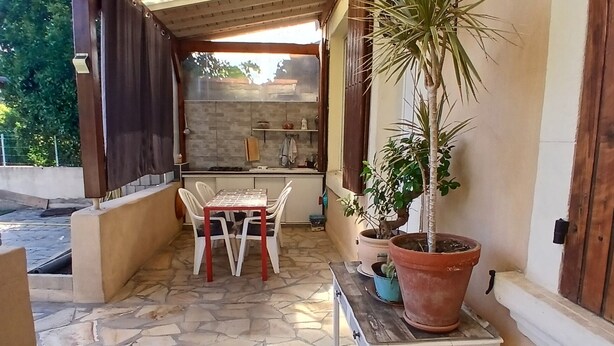 Un patio cubierto con suelo de piedra, una mesa y sillas, y plantas en macetas.