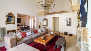 Uma sala de estar ampla com lustre, sofás, mesa de centro e lareira.