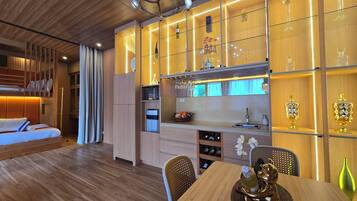 Quarto de hotel moderno com beliche, área de refeições com mesa e cadeiras, cozinha com pia e espaço para armazenamento de vinho, e um vaso decorativo na mesa.