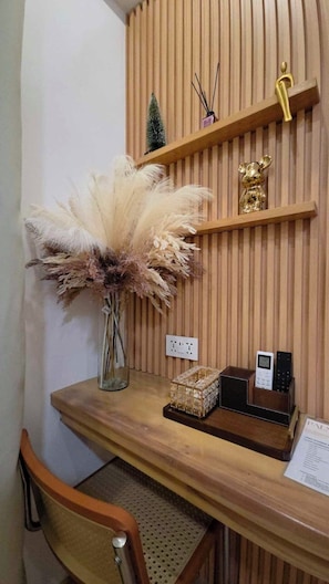 A wooden desk with a vase of pampas grass, a small Christmas tree, a golden mouse figurine, a remote control, and a glass cube.