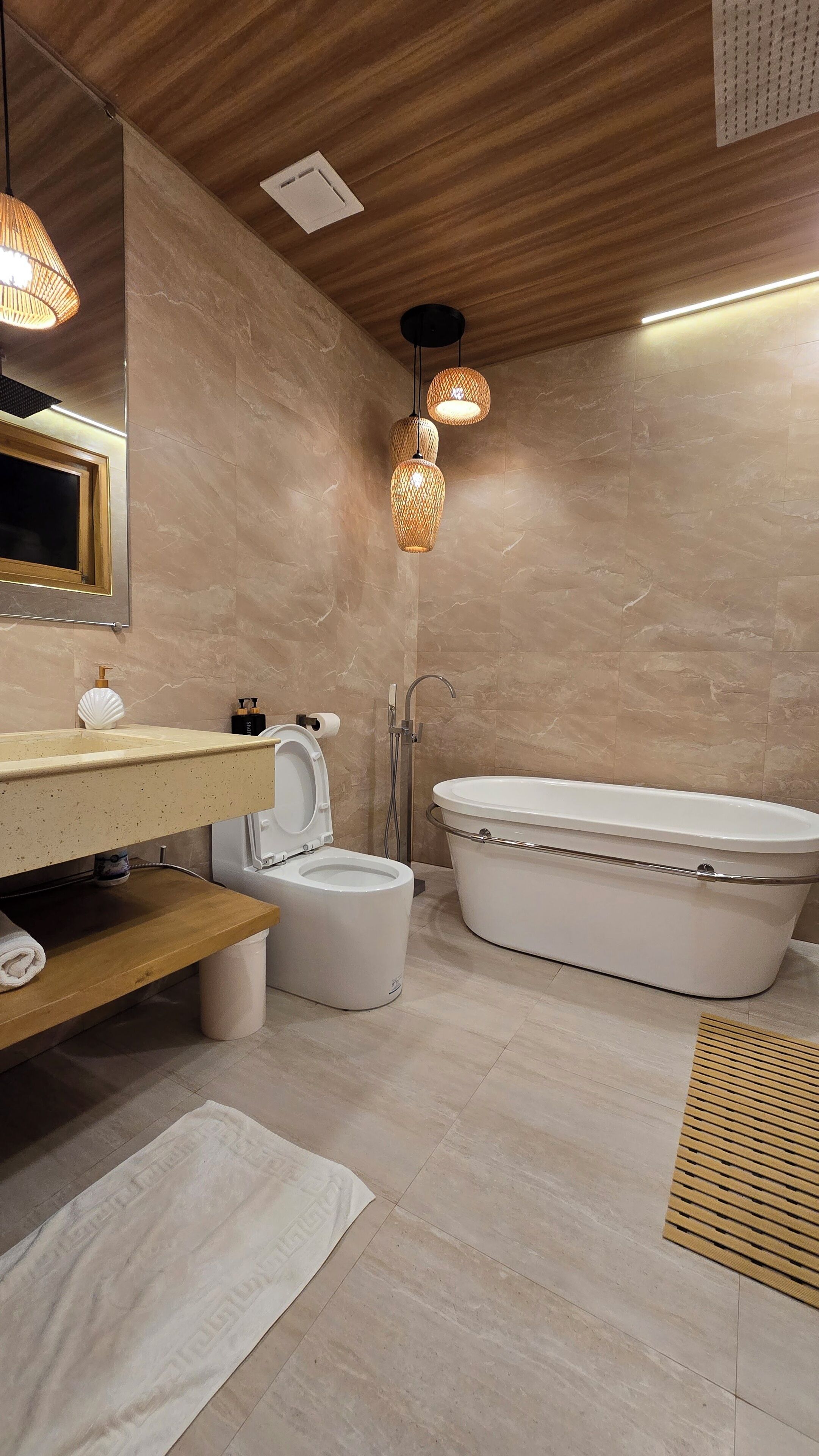 A modern bathroom with a freestanding bathtub, a toilet, a sink with a mirror, and two hanging light fixtures.