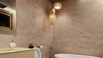 A modern bathroom with a freestanding bathtub, a toilet, a sink with a mirror, and two hanging light fixtures.