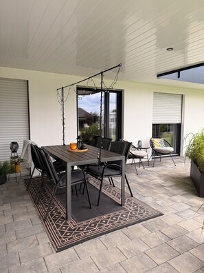 A patio with a table and chairs, a potted plant, and a view of the outside.