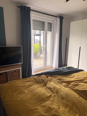 Ein Schlafzimmer mit Bett, Fernseher, Kleiderschrank und einer Glastür zum Balkon.
