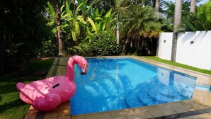 Una piscina amb un flamarosc flotant rosa, envoltada de vegetació exuberant i palmeres.