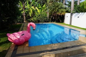 Uma piscina com um flutuador em formato de flamingo rosa, rodeada por vegetação exuberante e palmeiras.