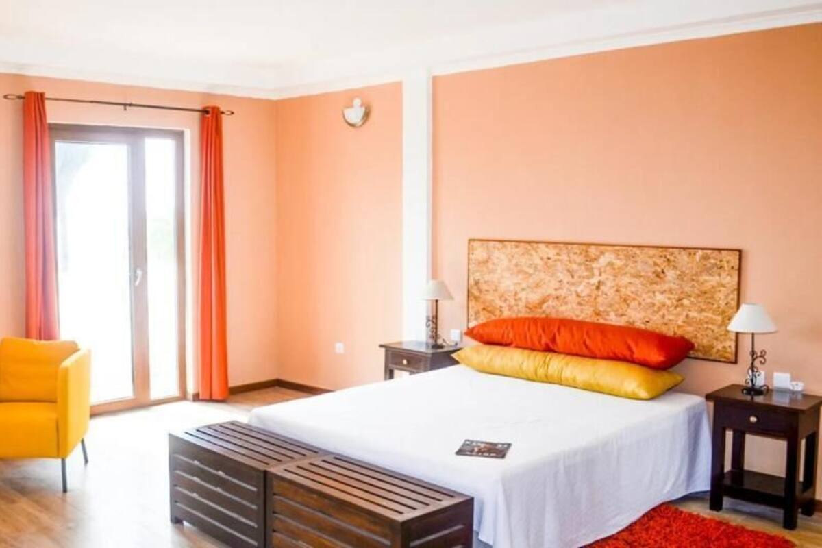 A hotel room with a bed, two chairs, a nightstand, a lamp, and a window with curtains.