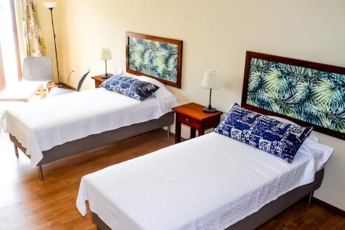 A hotel room with two single beds, a desk, a chair, a lamp, and a large window with curtains.