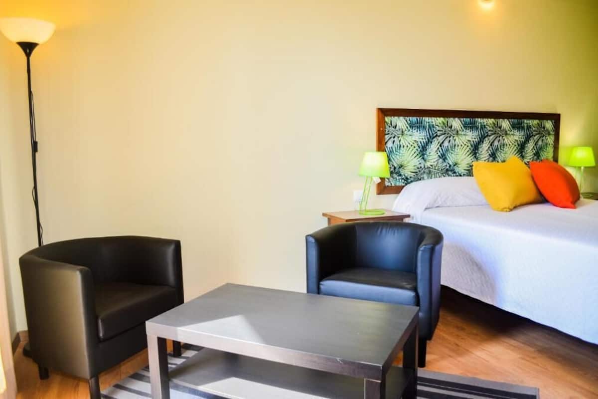 A hotel room with a bed, two chairs, a table, and two lamps.