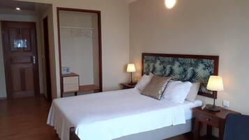A hotel room with a bed, bedside lamps, a nightstand, a mirror, and a door.