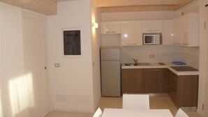A compact kitchen with a refrigerator, microwave, and sink, wooden cabinets, and a small window. - Two-story terraced home near the shores in Bibione (Bibione)