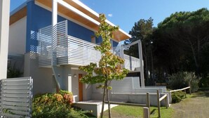 A modern building with a flat roof, large windows, and a small tree in the foreground. - Two-story terraced home near the shores in Bibione (Bibione)