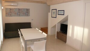 Un espace repas comprenant une table et des chaises, un canapé, un téléviseur et un escalier menant à un autre niveau.