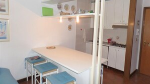 Una cocina compacta con armarios blancos, una pequeña isla con taburetes y un comedor con una silla azul.