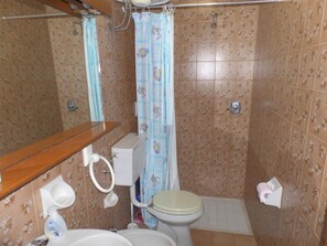 Un baño con inodoro, lavamanos, cortina de ducha y paredes de azulejos.