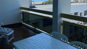 Un balcón con mesa y sillas, vista al mar y un edificio de fondo.
