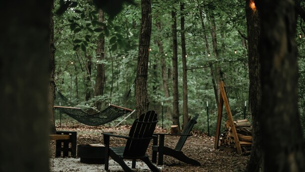 A hammock, a chair, and a small table in a forest setting.
