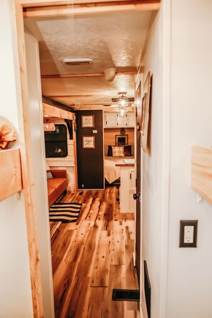 A narrow hallway with wooden flooring, a bed, a small seating area, and a kitchenette. - Boho Farmhouse Camper with AC in Harpers Ferry (Harpers Ferry)