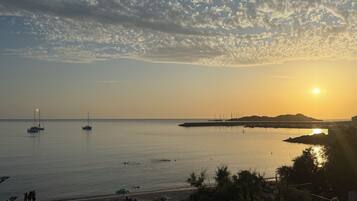 Paisaje costero con barcos, una playa y un atardecer.
