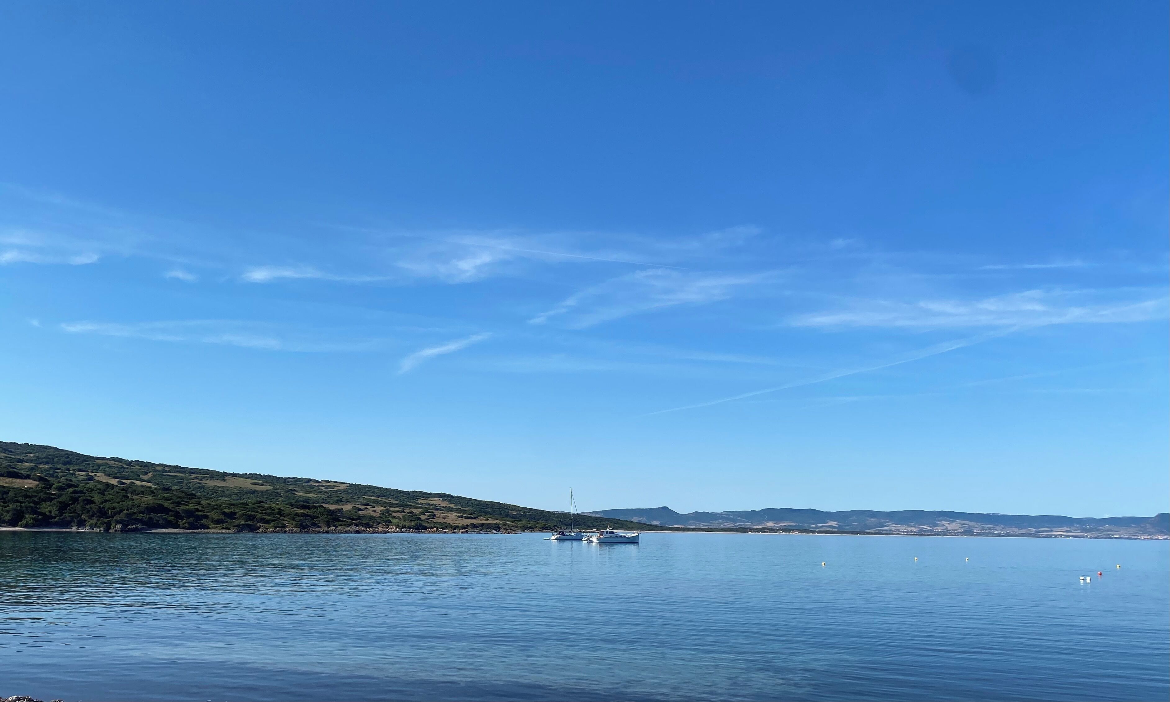 Un lago tranquilo con barcos, cielo despejado y un paisaje montañoso.