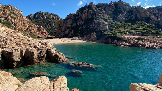 A coastal landscape with clear turquoise water, rocky terrain, and a small building on the beach. - Residence La Marina (Isola Rossa)