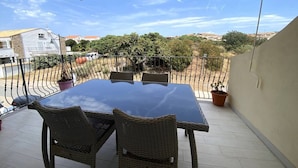 A covered balcony with a table and chairs, potted plants, and a view of the neighborhood. - Residence La Marina (Isola Rossa)