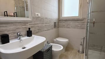 Une salle de bain dotée d’un grand miroir, d’un lavabo, d’un bidet, de toilettes et d’une douche à parois de verre.