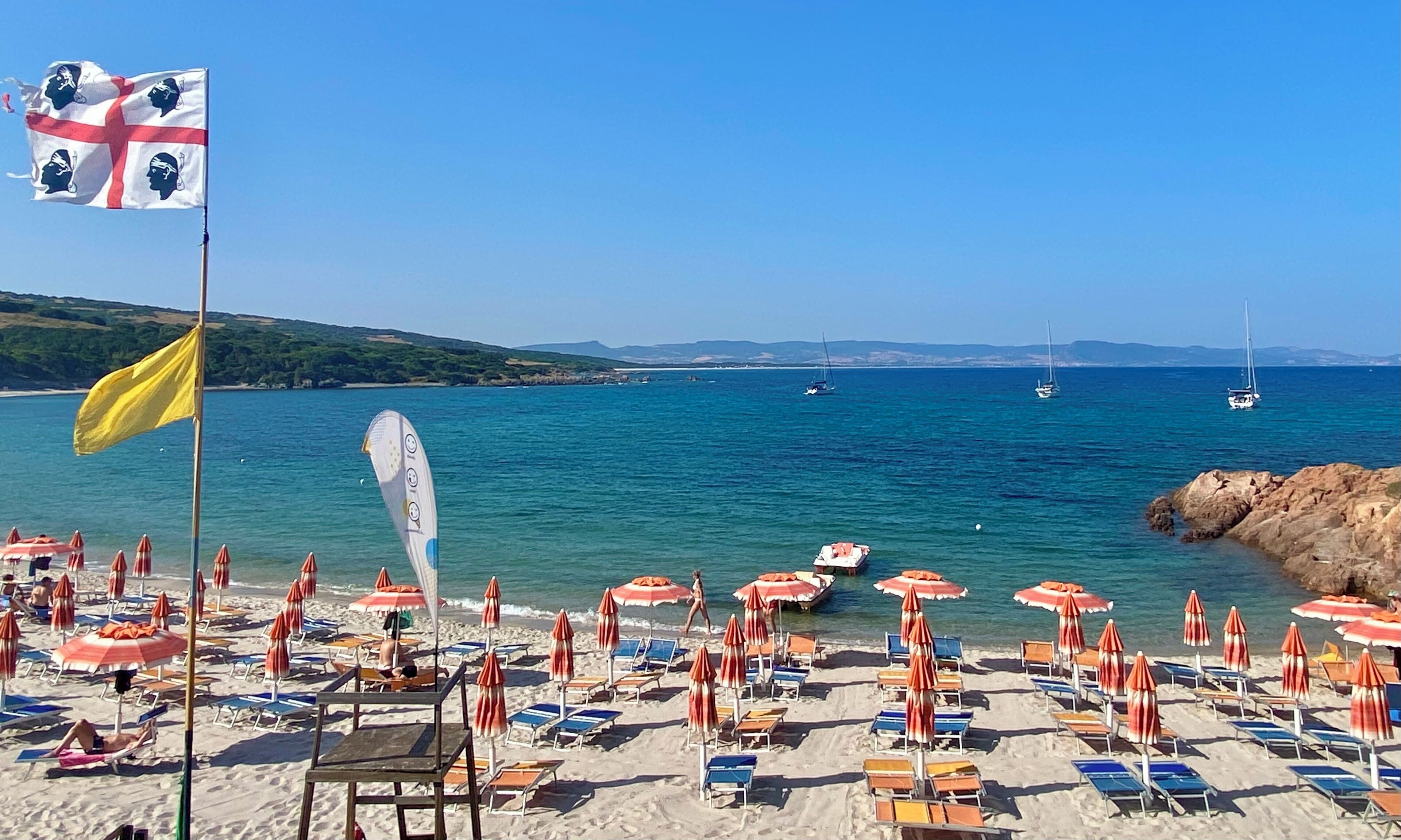 Une plage avec des parasols, des chaises longues et un drapeau.