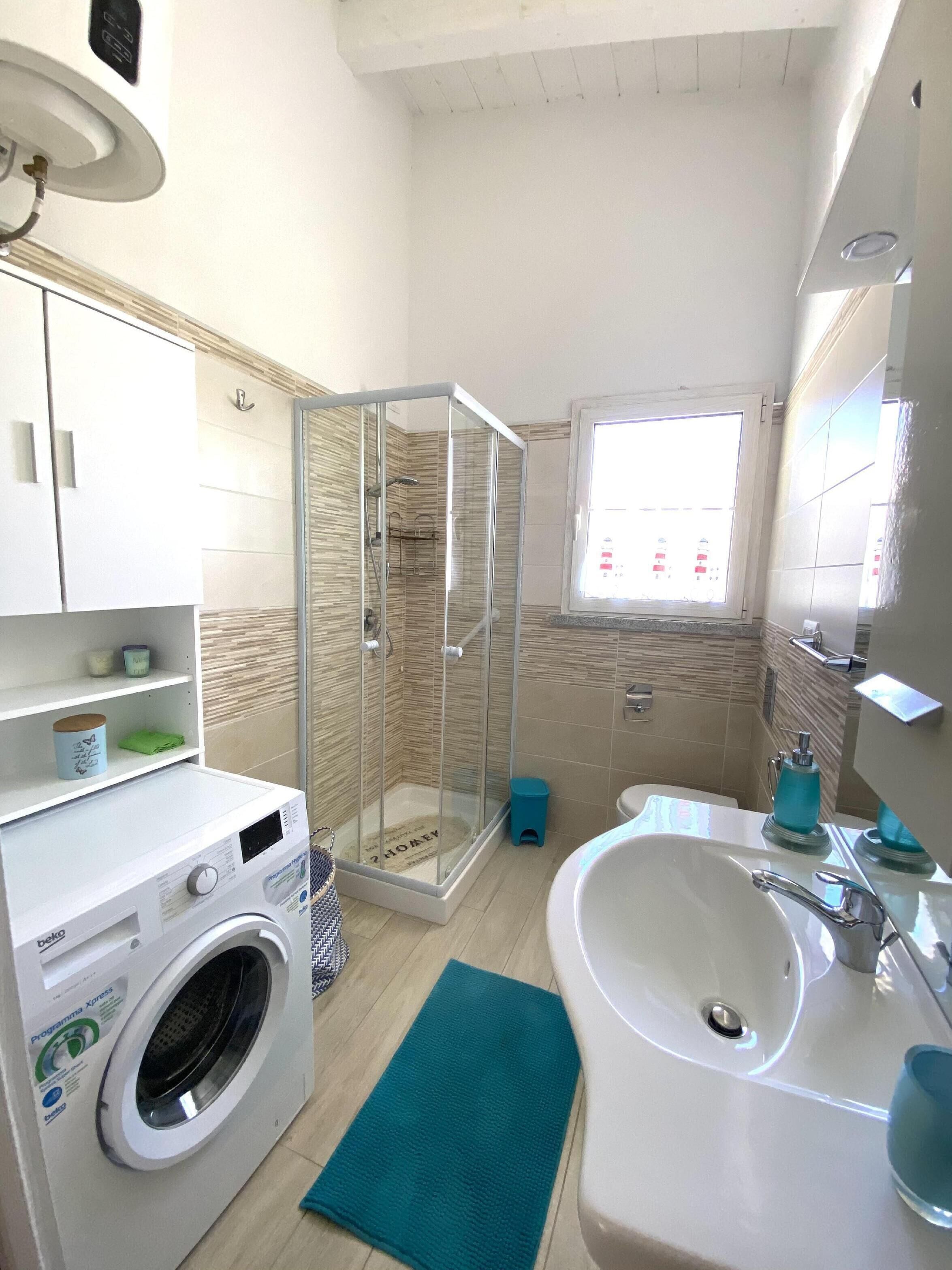 Un baño compacto con lavadora, cabina de ducha de cristal, lavamanos y ventana.