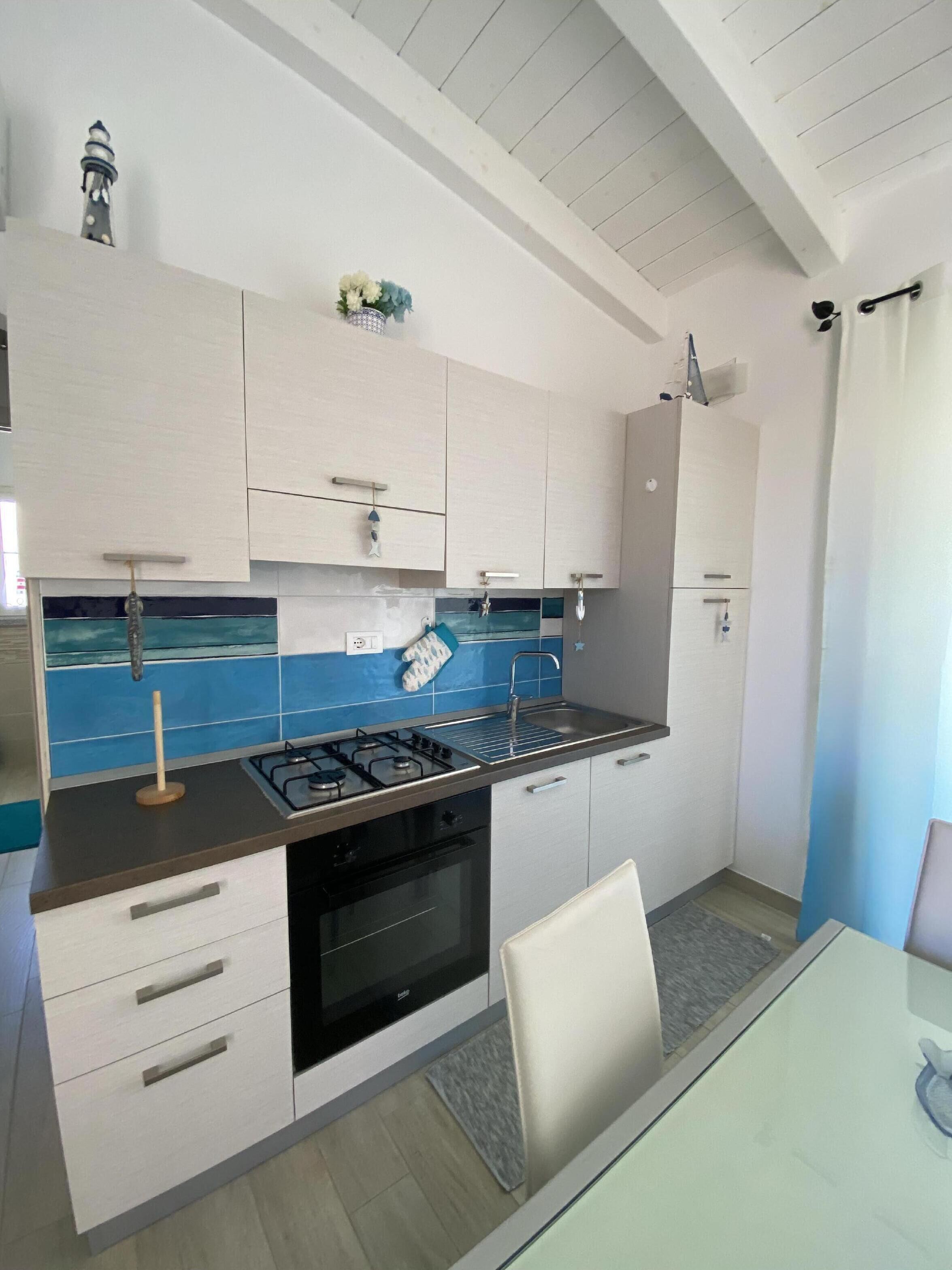 A modern kitchen with white cabinets, a blue backsplash, and a gas stove.