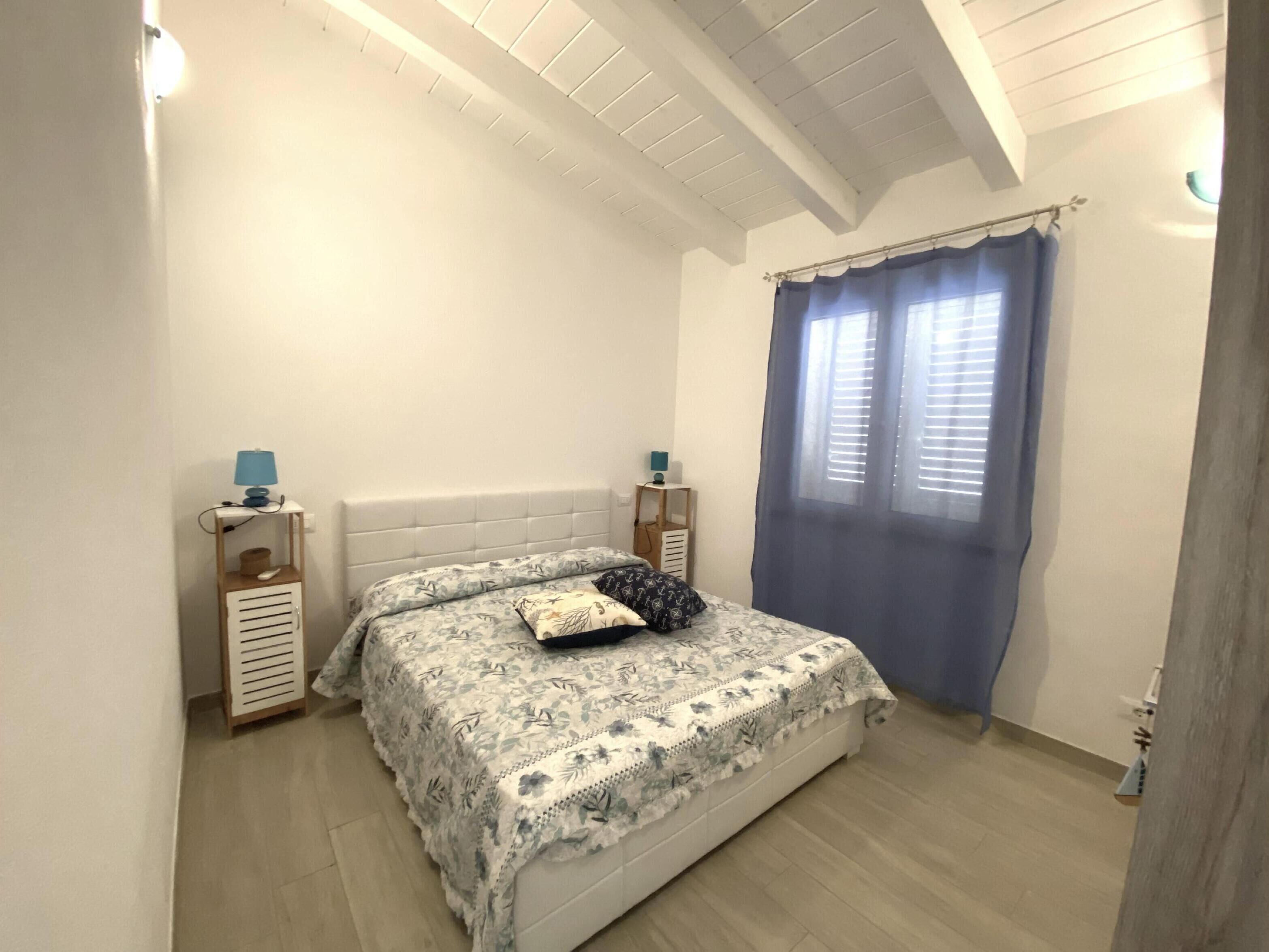 A bedroom with a bed, a nightstand, a lamp, and a window with curtains.