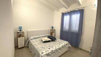 A bedroom with a bed, a nightstand, a lamp, and a window with curtains.